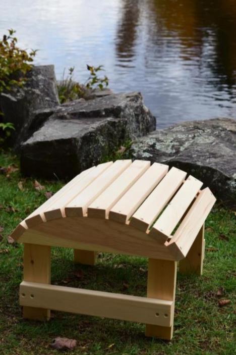 Handcrafted wooden ottoman placed on a grassy lakeside setting, featuring a slatted curved design for comfort and rustic outdoor charm