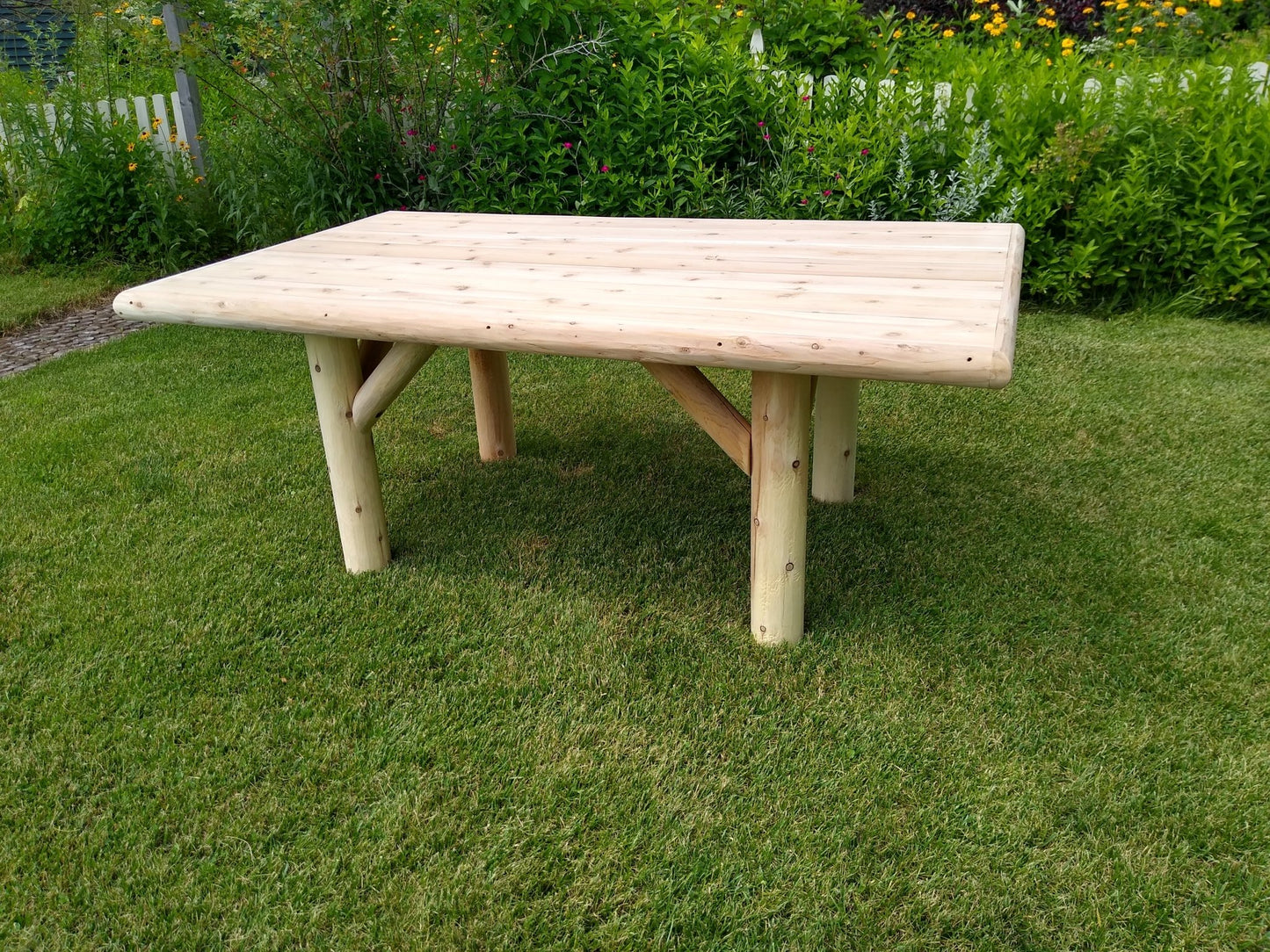 Rustic outdoor dining table with a handcrafted wooden design, placed on a grassy lawn surrounded by greenery.