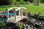Wooden Decorative Garden Bridge over a small pond, surrounded by rocks, greenery, and flowers in a backyard.