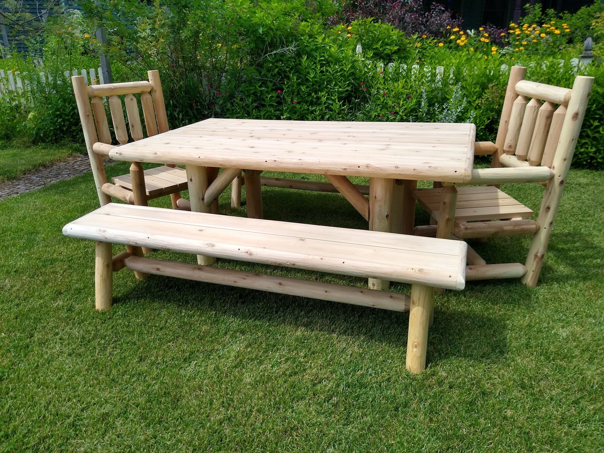 Rustic outdoor farmhouse table and chairs set with a matching bench on a lawn, perfect for alfresco dining.