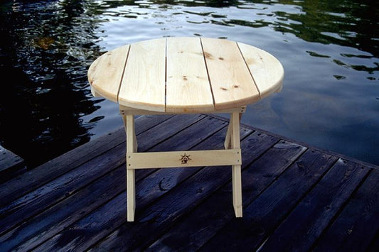 Farmhouse round wood coffee table with a natural finish, placed on a dock overlooking a serene lake.